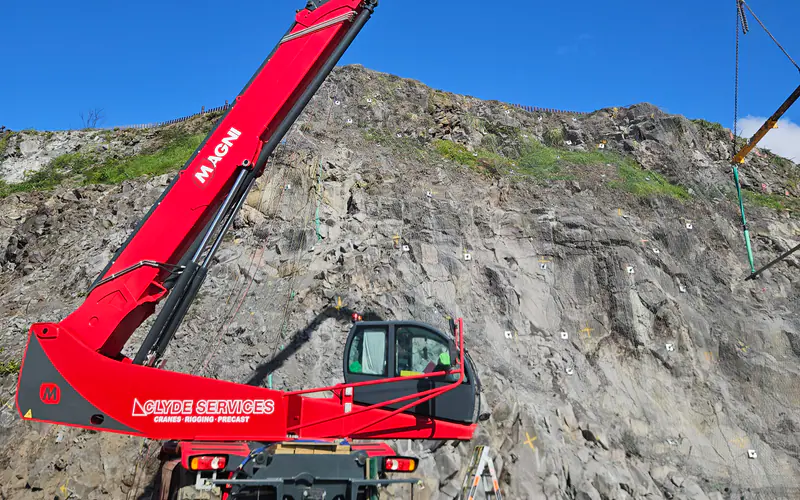 Crane lifting protection materials below a volcanic rock face