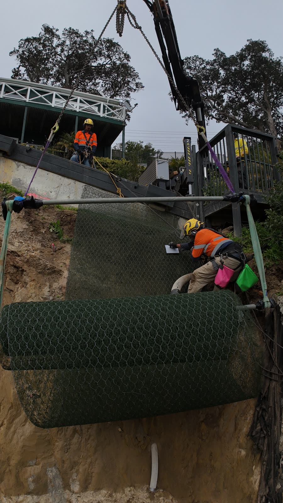 Rope access technician securing rockfall mesh on a slope face